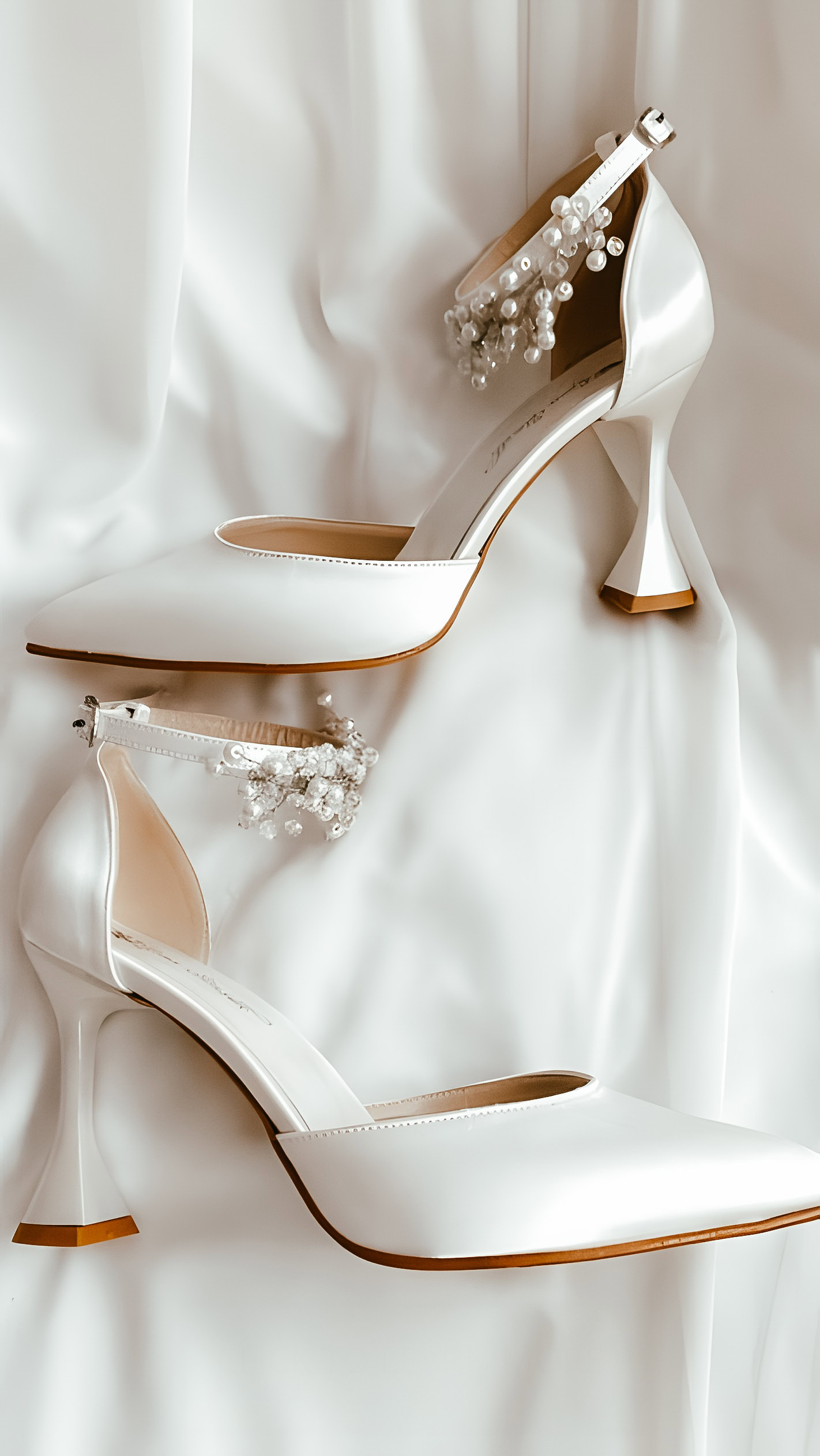Elegante weiße Hochzeitsschuhe mit hohem Absatz und Schmuckdetails, auf seidigem Stoff fotografiert. Perfekte Hochzeitsfotografie und Videografie in Frankfurt, stilvoll und detailreich festgehalten.